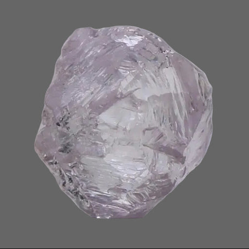 A single rough, uncut purple Pink Diamond against a  light gray background.