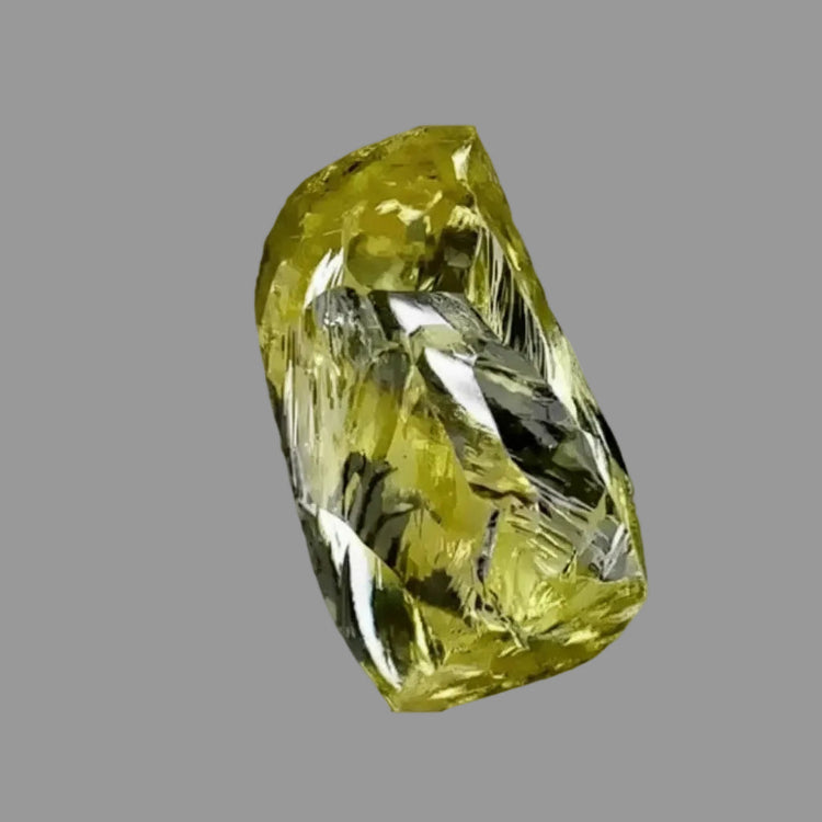A rough clear yellow diamond, shown against a gray background.